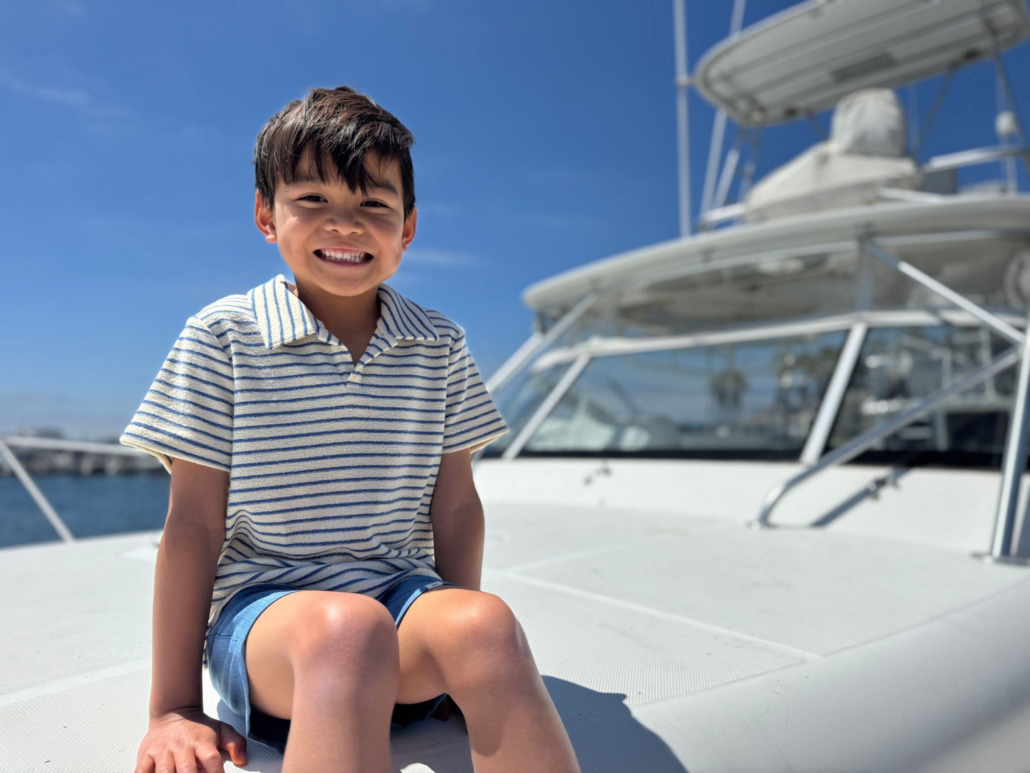Child sitting on a boat with a clear blue sky and water in the background
