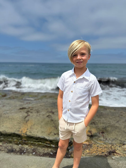 Young boy standing on a rocky beach with ocean waves in the background