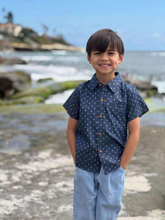Child wearing a navy blue shirt with white patterns and light blue pants standing on a beach.