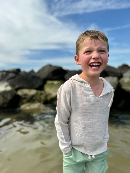 Child laughing on a beach with rocks and blue sky in the background