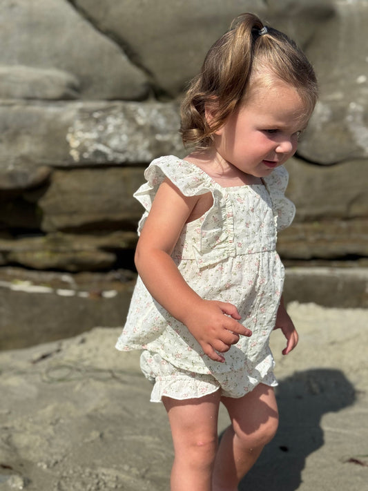 Young child in a white floral dress standing on a rocky surface.