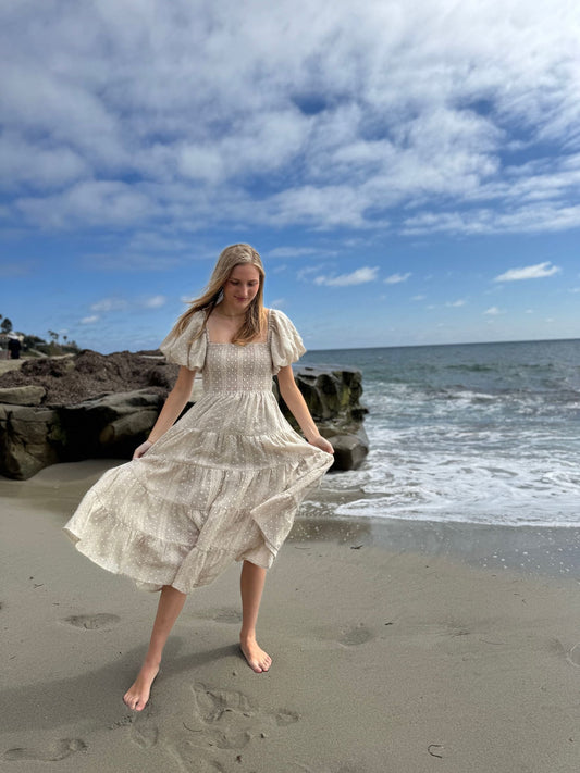 Woman in a white dress standing on a beach with ocean and sky in the background