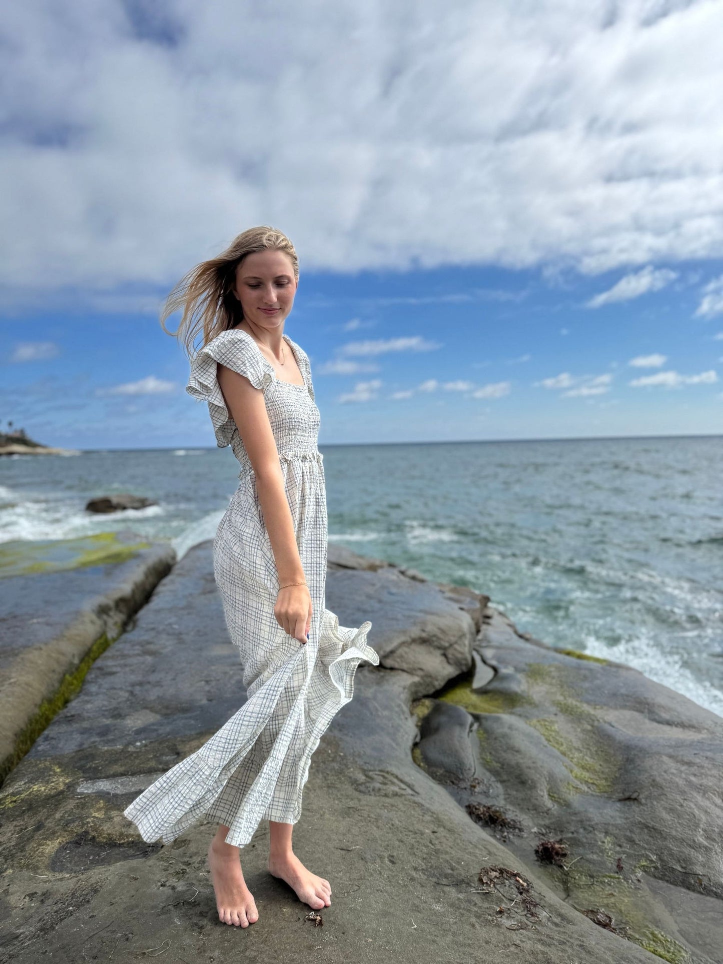 Woman in a white dress standing on a rocky beach with ocean and sky in the background