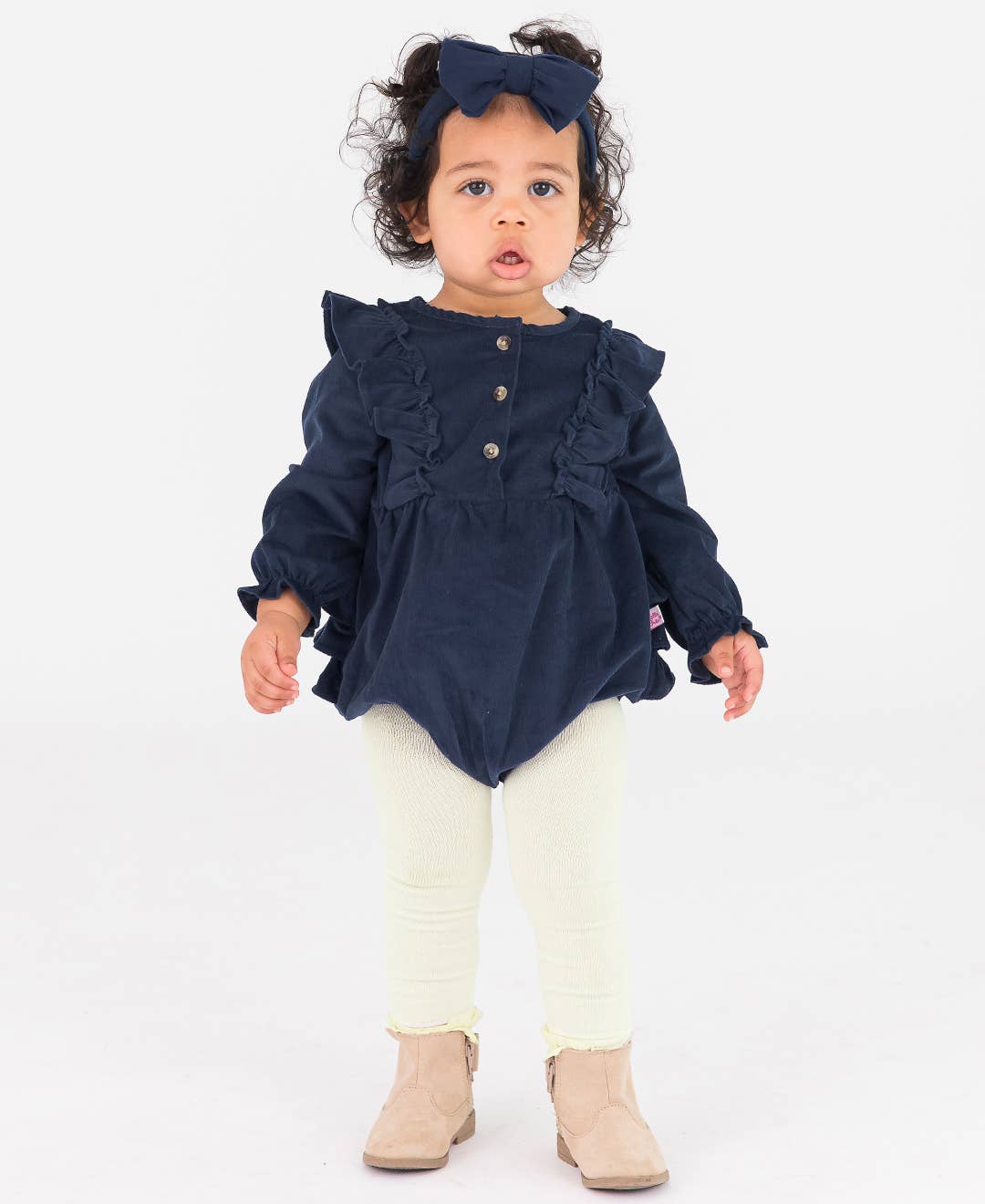 Child wearing a navy blue top with ruffles and white pants on a white background