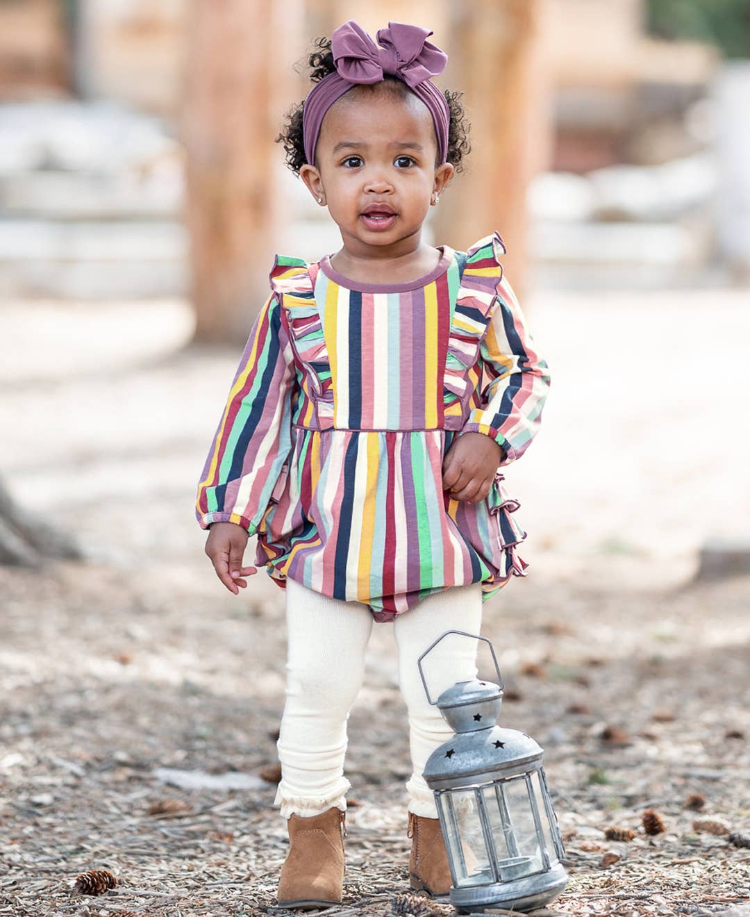 Child wearing a colorful striped shirt and holding a lantern outdoors.