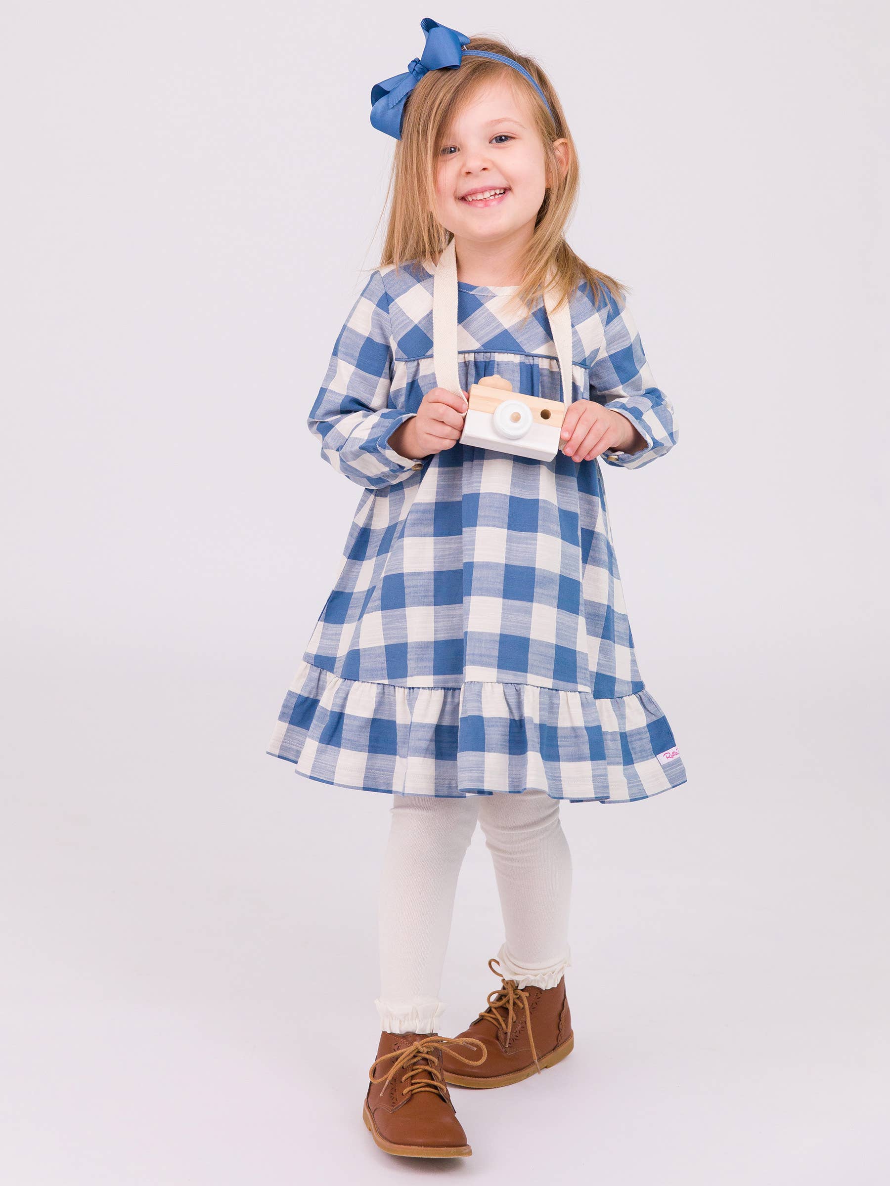 Young girl wearing a blue and white checkered dress with a bow in her hair on a white background