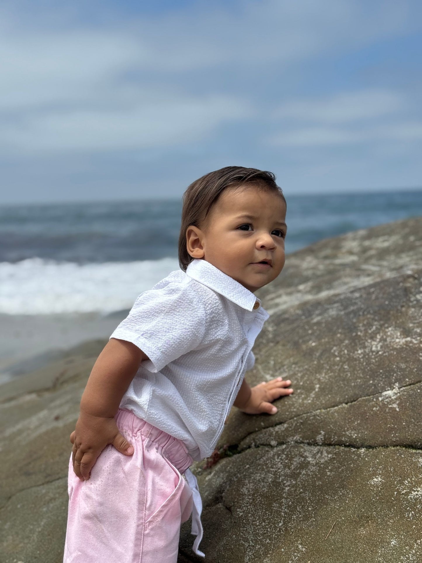 Child standing on a rock by the ocean with waves crashing in the background