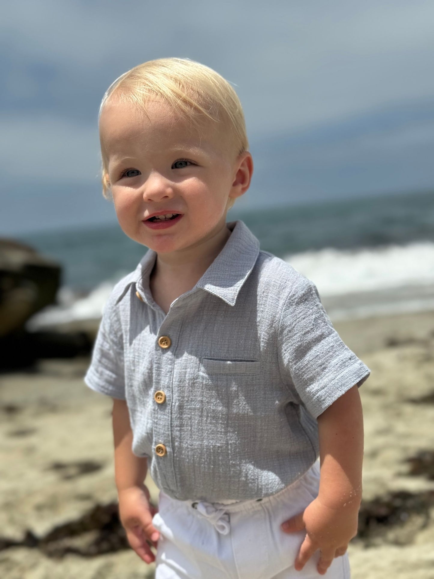 Child in a light gray shirt with gold buttons on a beach