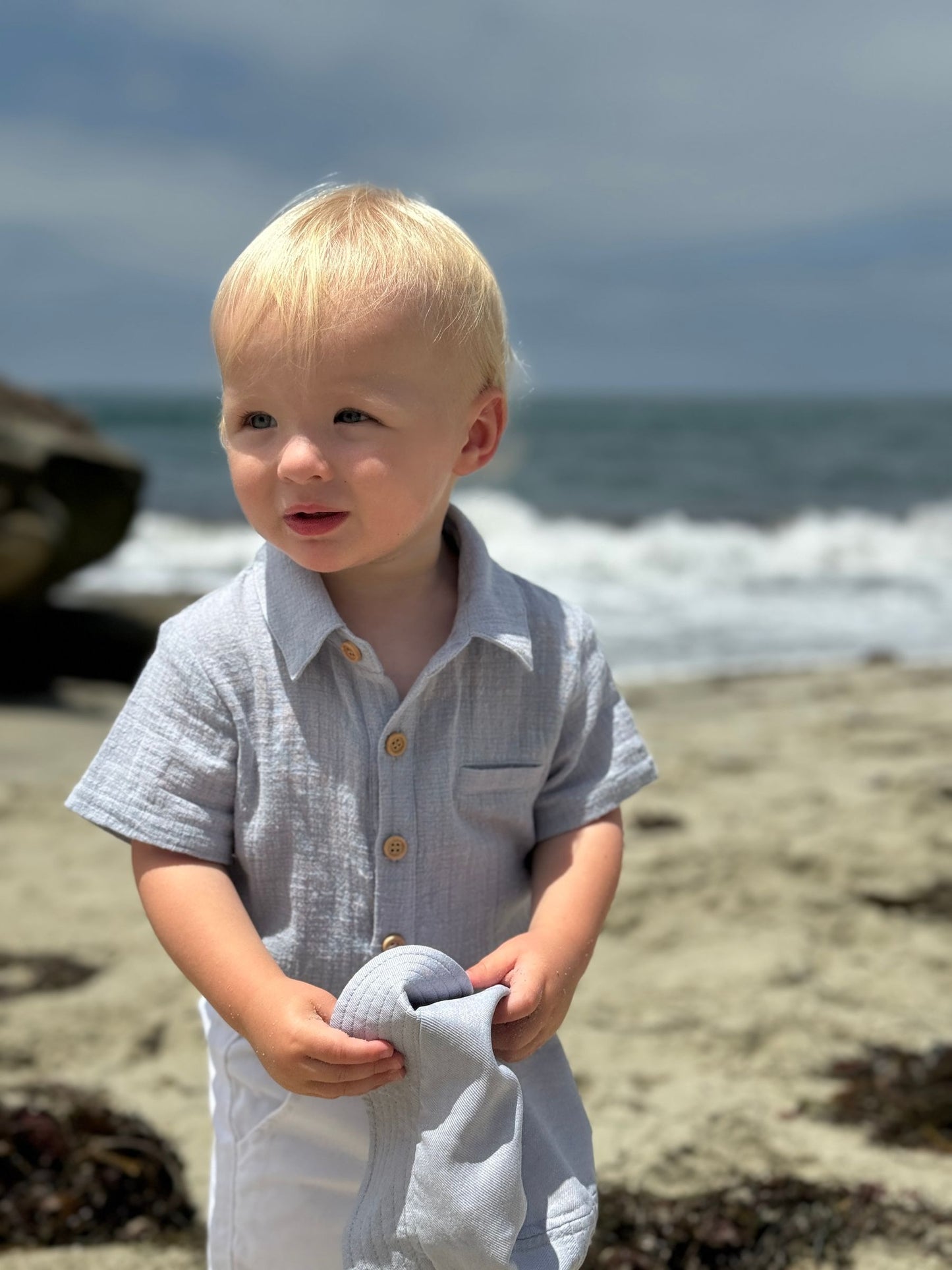 Child standing on a beach holding a towel with ocean waves in the background