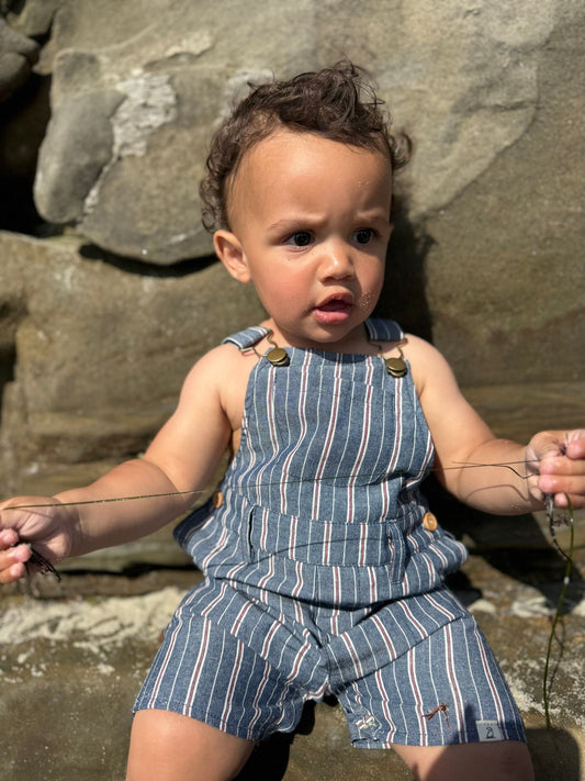 Child wearing a blue striped outfit sitting on rocks.