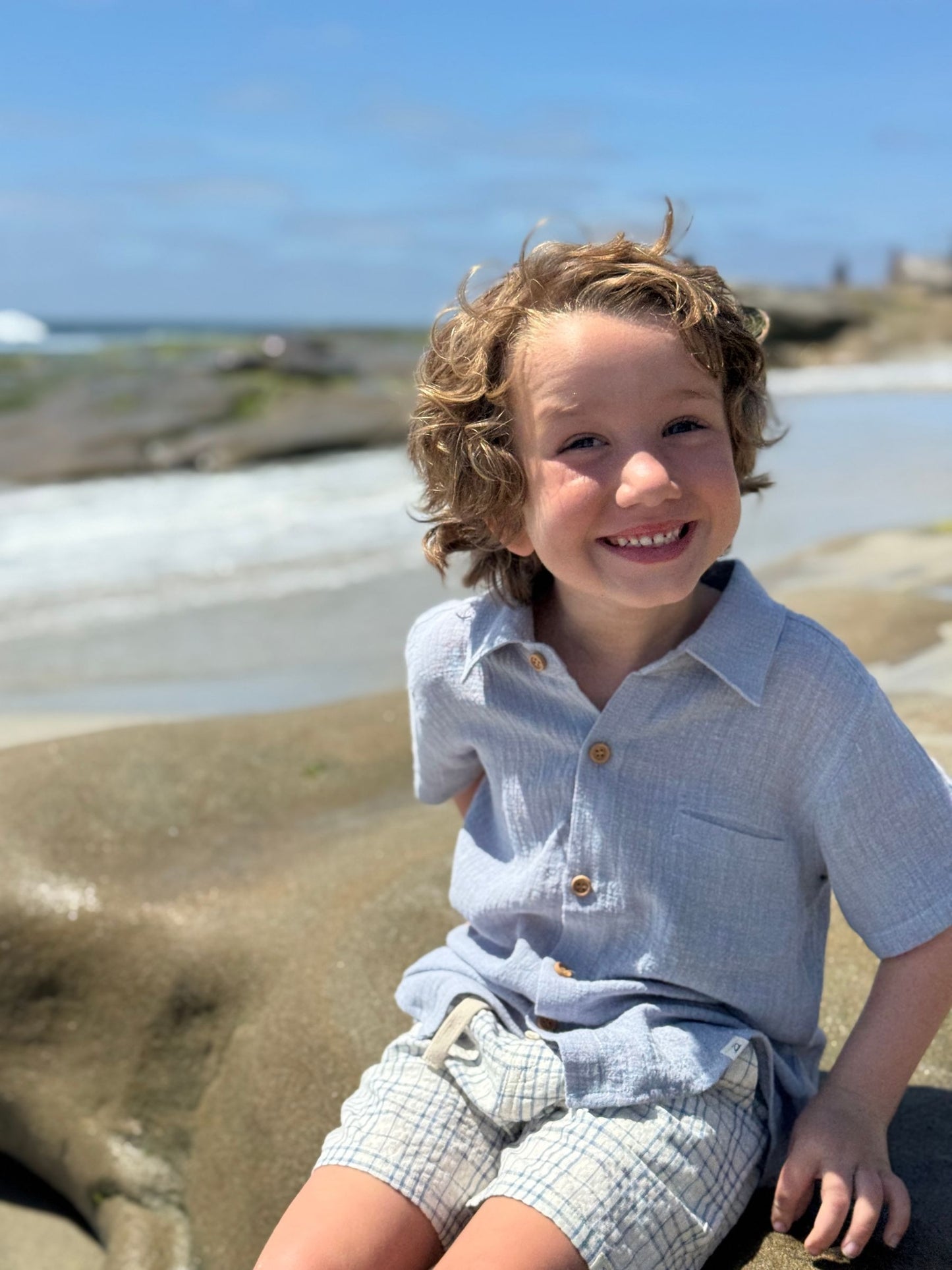 Child sitting on a sandy beach with a clear blue sky.