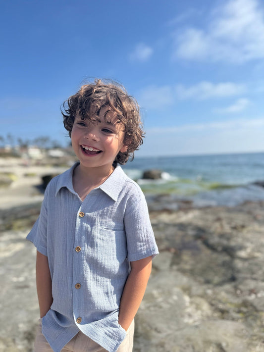 Child standing on a rocky beach with ocean and clear blue sky in the background