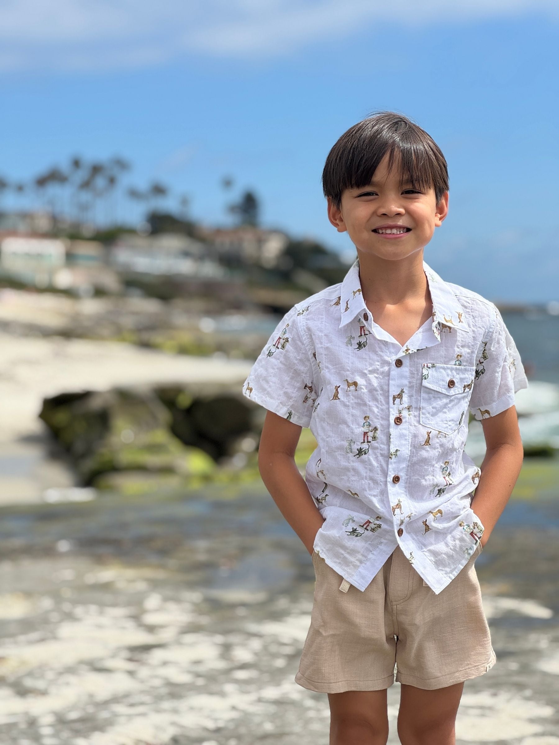 Child wearing a patterned shirt and beige shorts standing on a beach with a blurred background