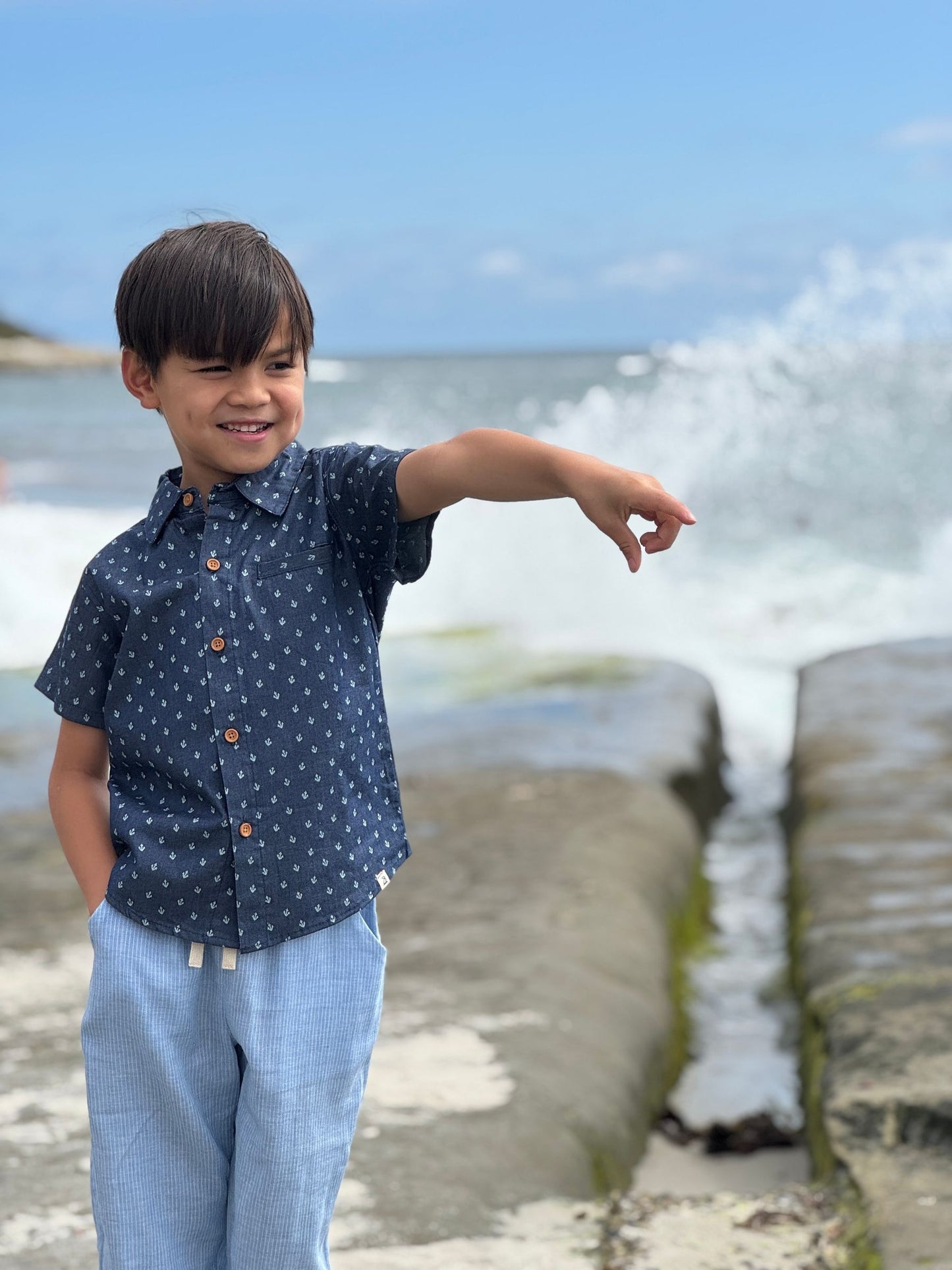Child in a polka dot shirt and jeans standing on a beach with waves crashing behind