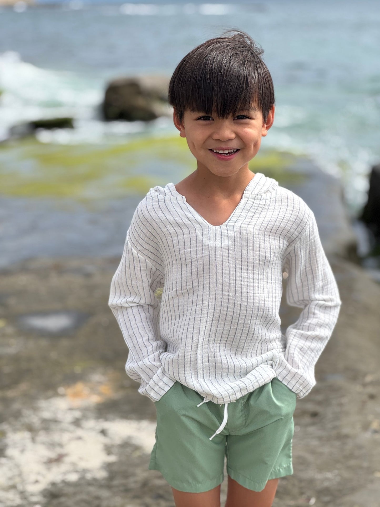 Child wearing a white shirt and green shorts standing on a rocky beach.