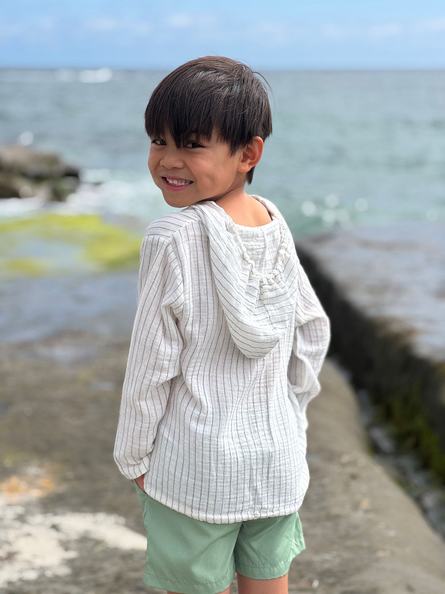 Child standing by the ocean wearing a white shirt and green shorts.