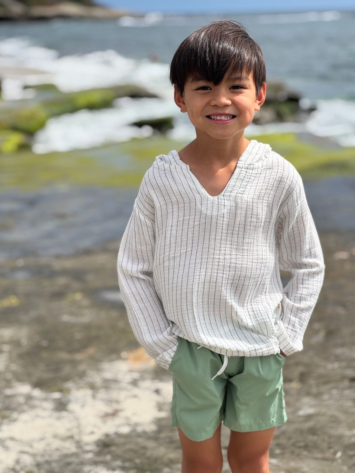 Child wearing a white shirt and green shorts standing on a rocky beach.