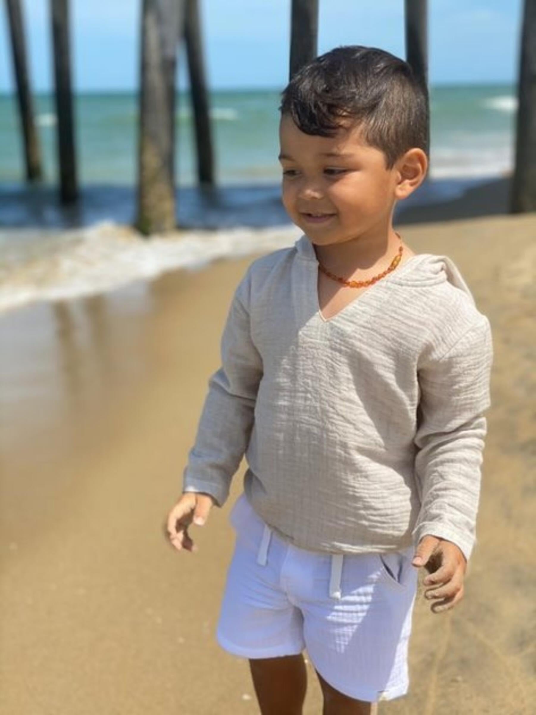 Child standing on a sandy beach with ocean and pier in the background