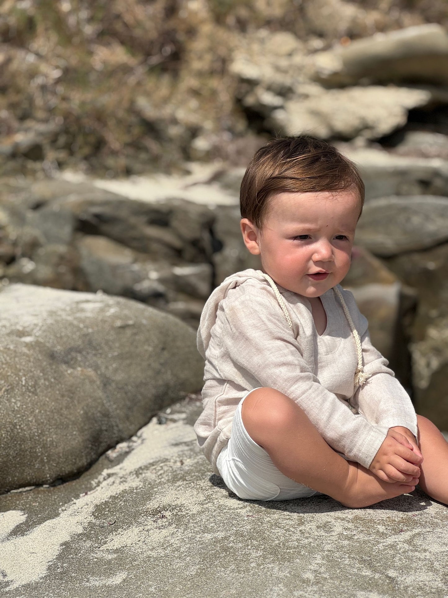 Child sitting on rocks wearing a light-colored outfit