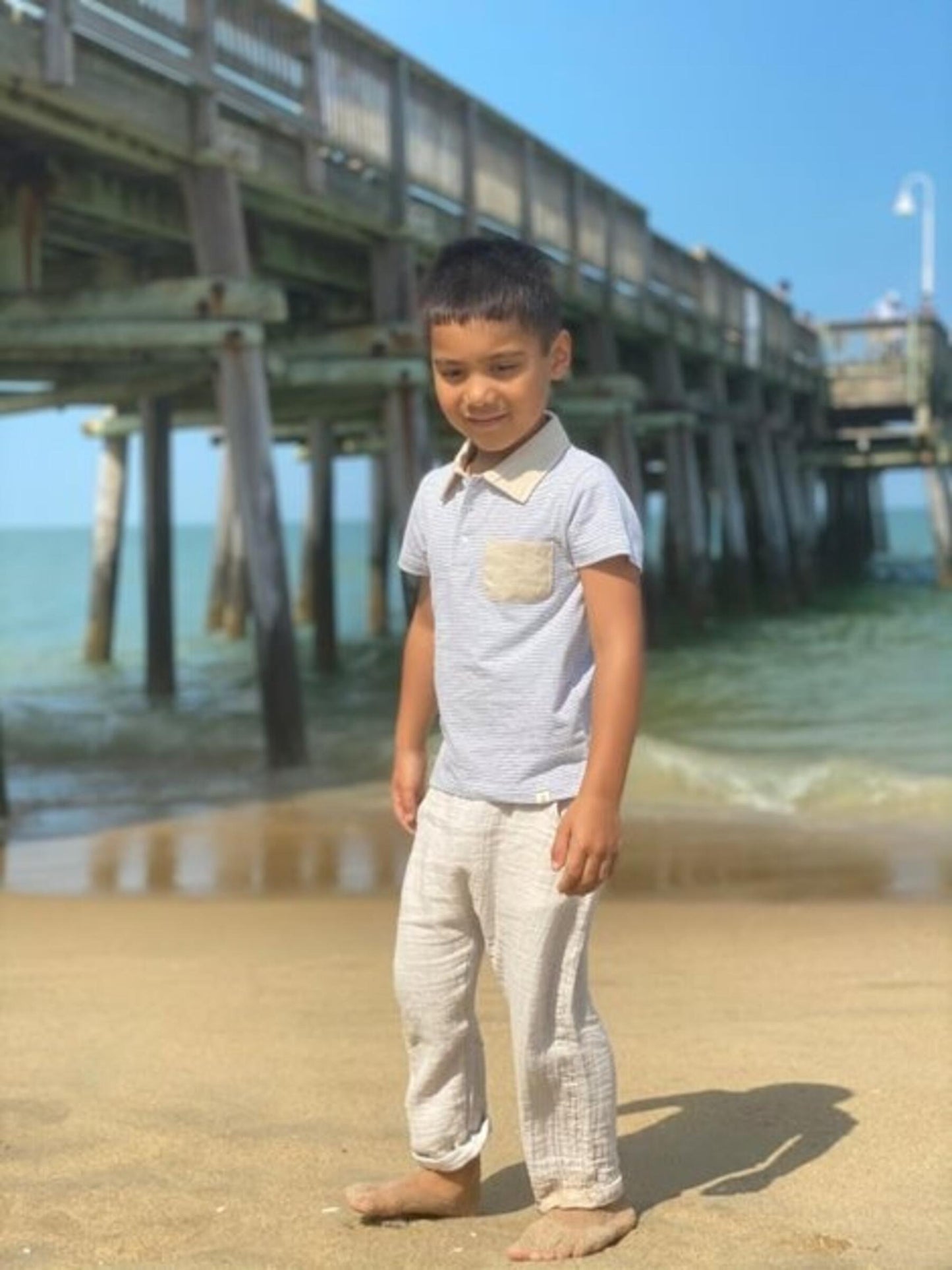 Child standing on a beach with a pier in the background
