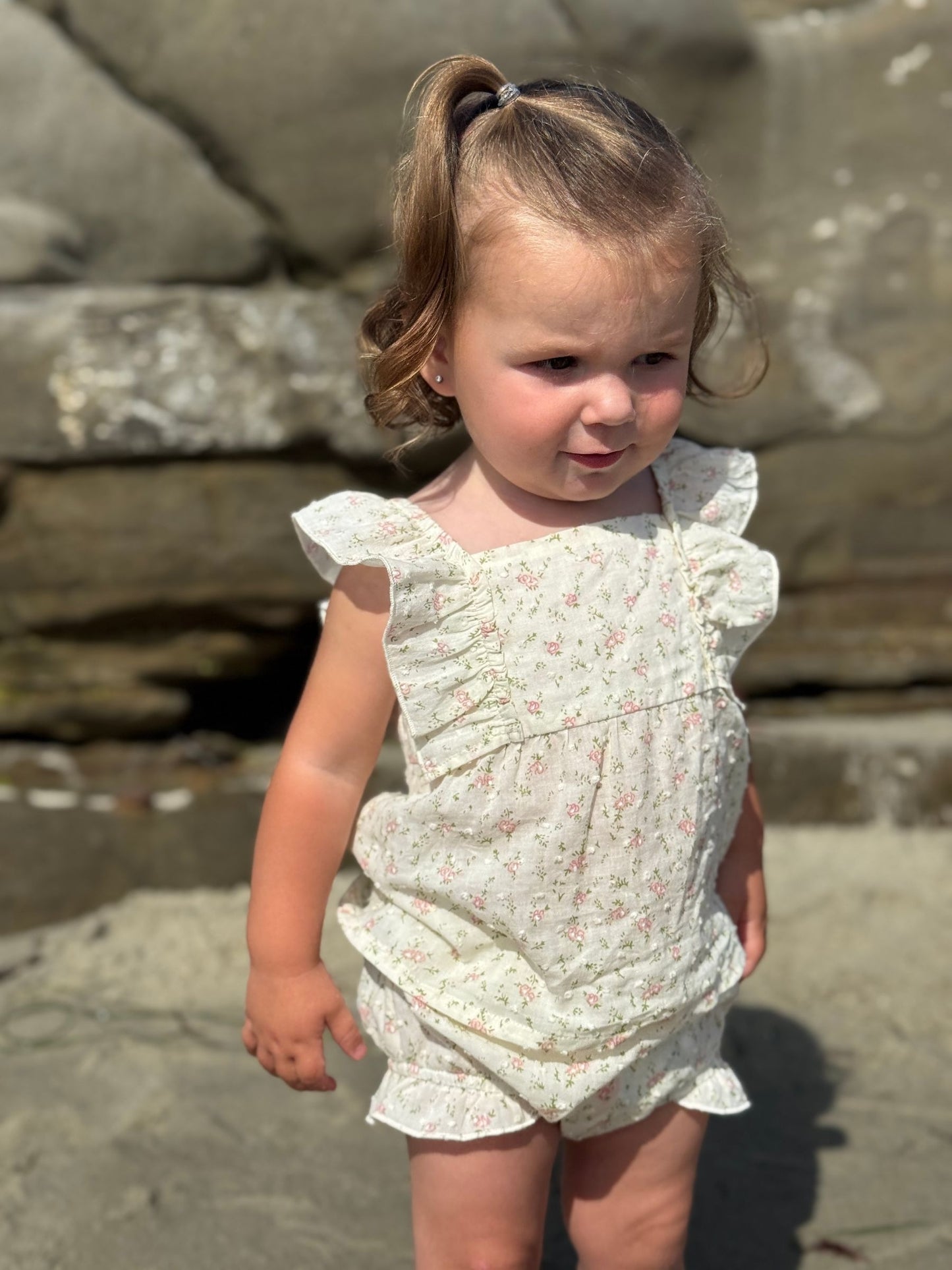 Young child in a white floral dress standing on a rocky surface.