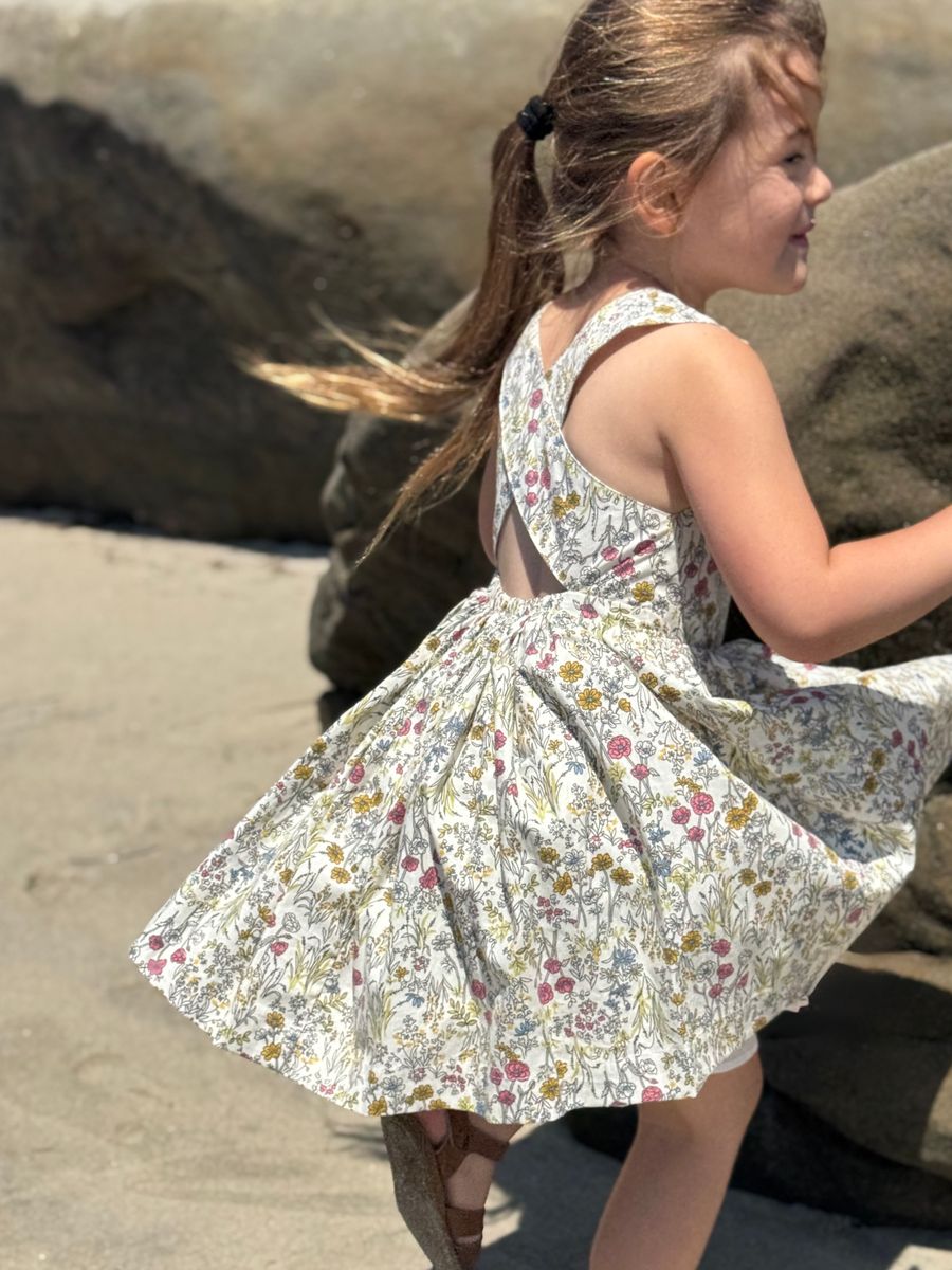 Young girl in a floral dress sitting on rocks by the beach