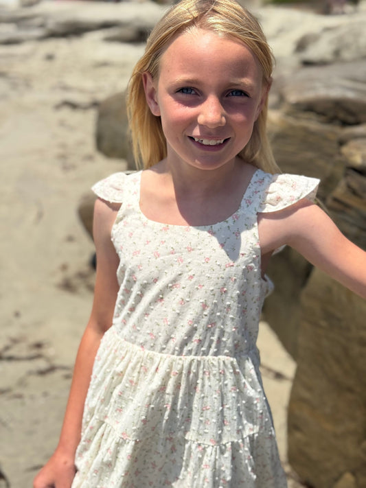 Young girl in a floral dress standing on a beach with rocks in the background