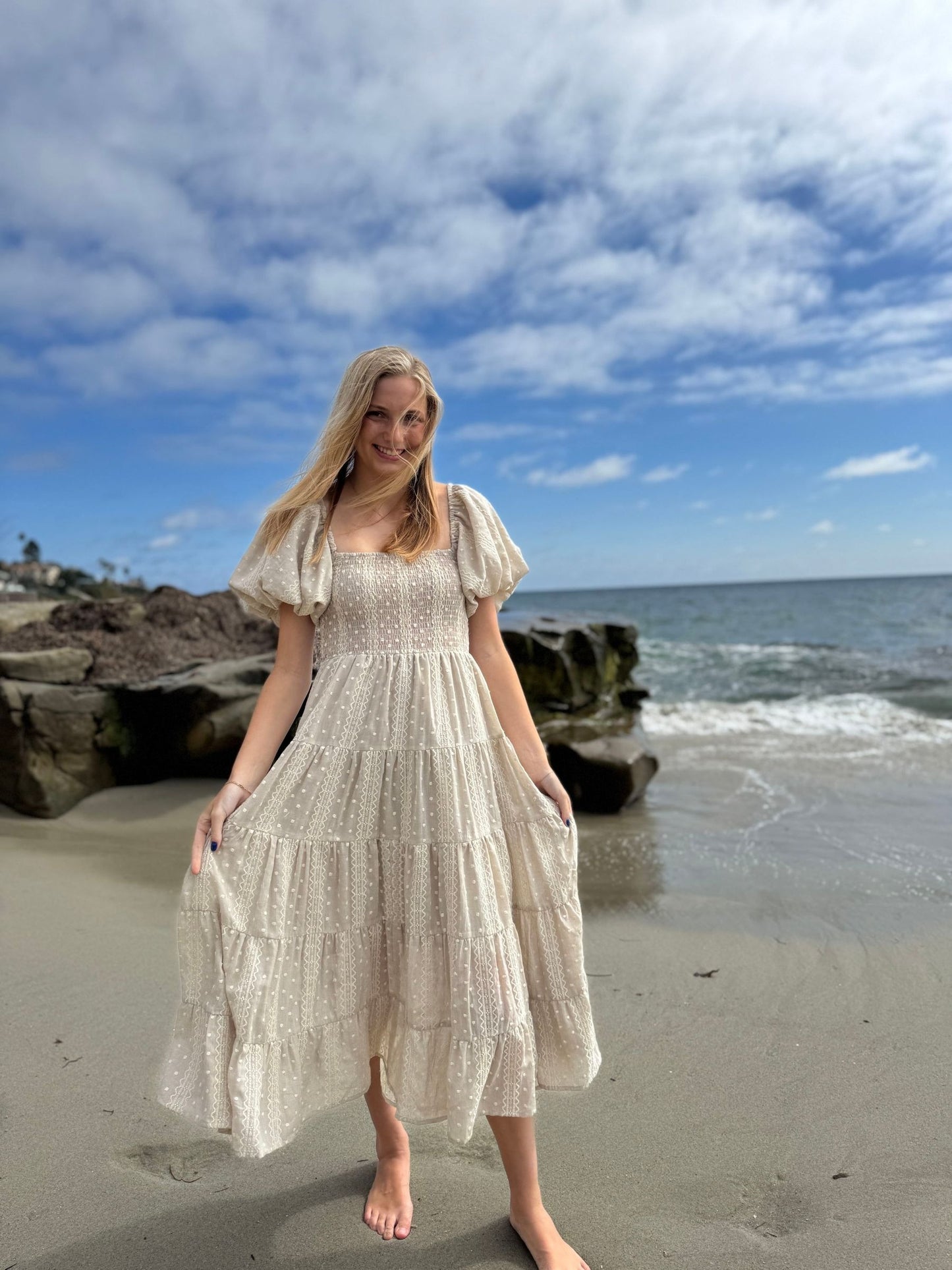 Woman in a beige dress standing on a beach with ocean and sky in the background