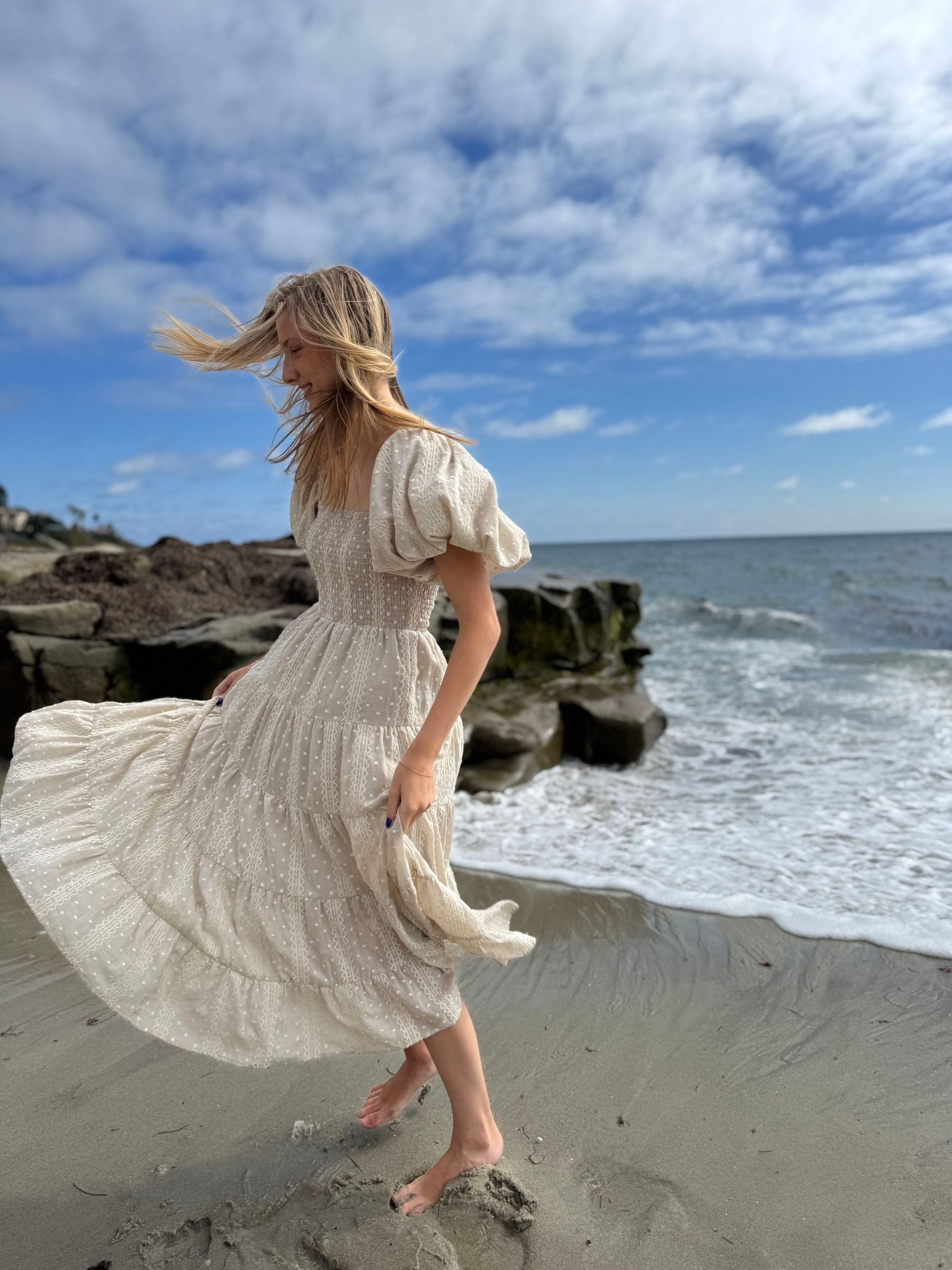 Woman in a flowing dress on a beach with ocean and sky in the background