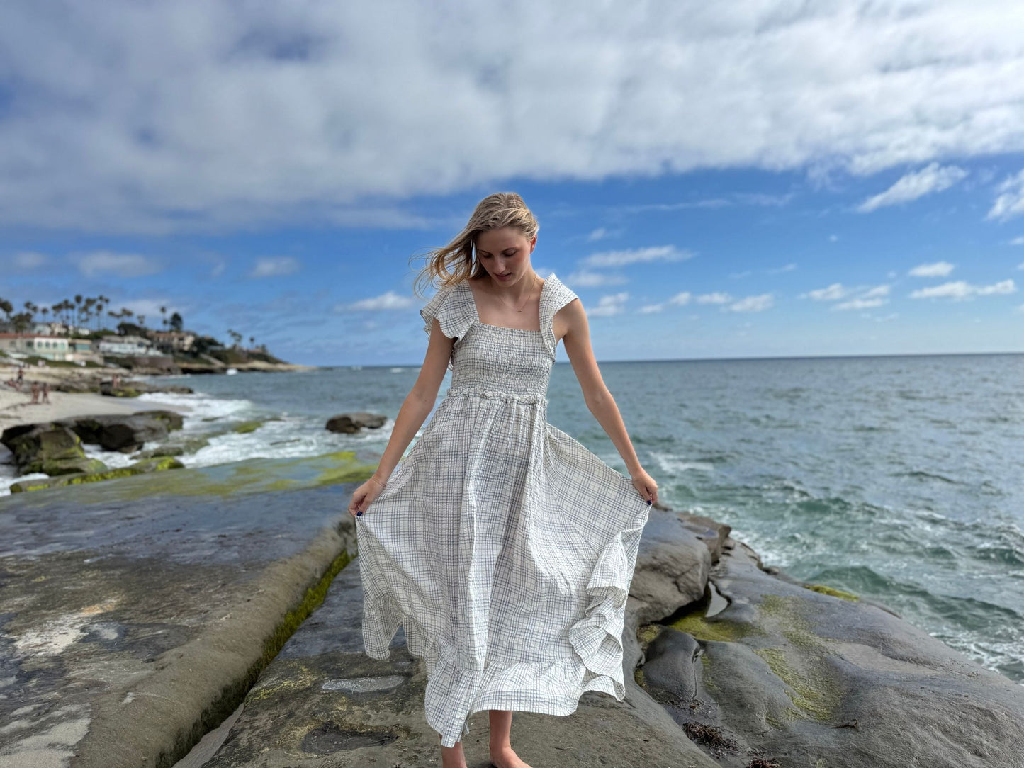 Woman in a white dress standing on a rocky beach with ocean and sky in the background