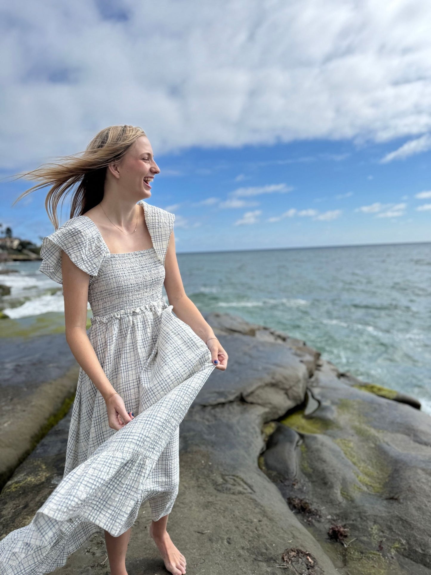Woman in a white dress standing on a rocky beach with ocean and sky in the background