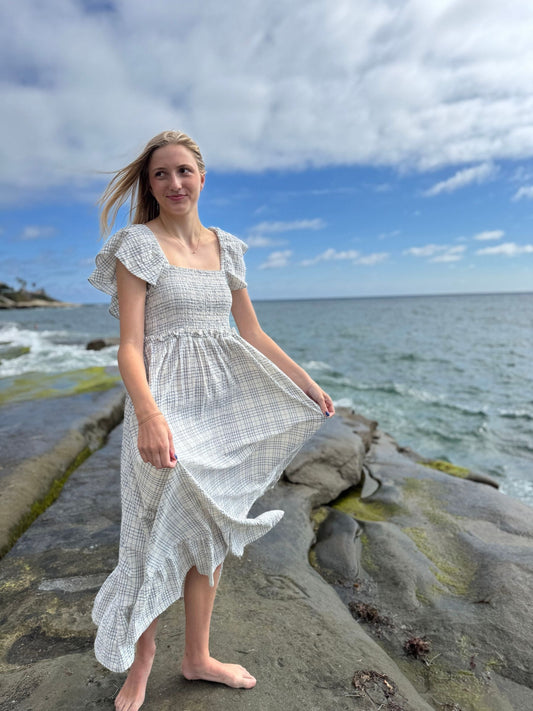 Woman in a white dress standing on a rocky beach with ocean and sky in the background