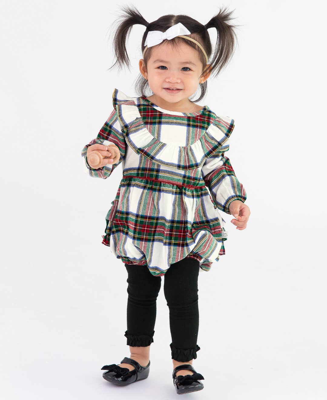 Child wearing a plaid dress with ruffles, and black ruffled footless tights on a white background