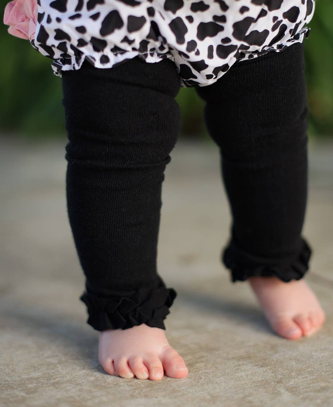 Close-up of a child's legs wearing black leggings with ruffled cuffs on a blurred background.